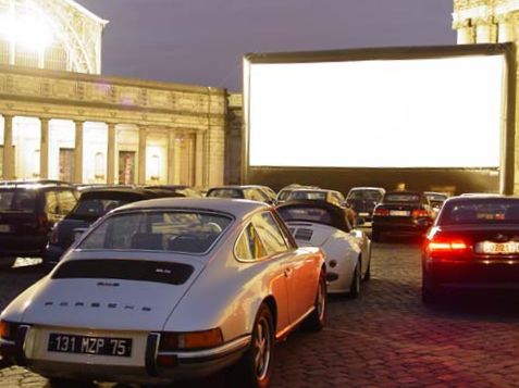 Mehrere Autos stehen vor einer weißen Leinwand auf einem Platz.