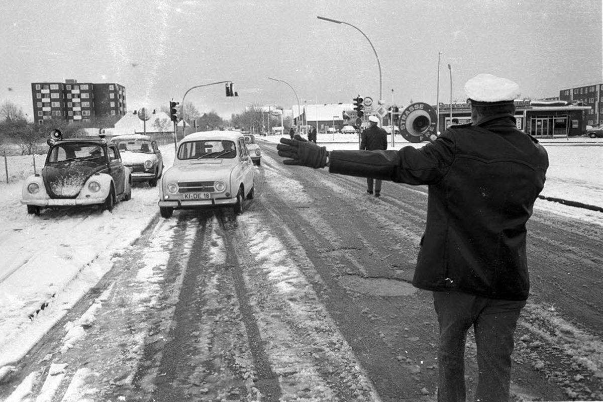 Sonntagsfahrverbot wegen der Ölkrise 1973 Zwei Verkehrspolizisten bringen Autos auf einer verschneiten Straße zum Halten.