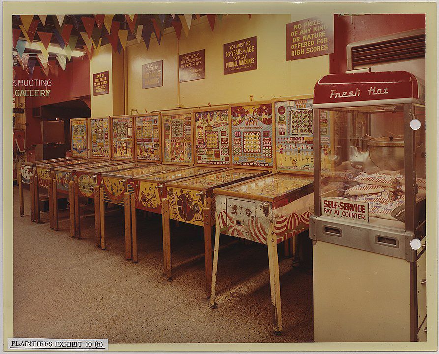 Fotografie vieler Spielautomaten an einer Wand aufgereiht. Danaben ein Popcornautomat.