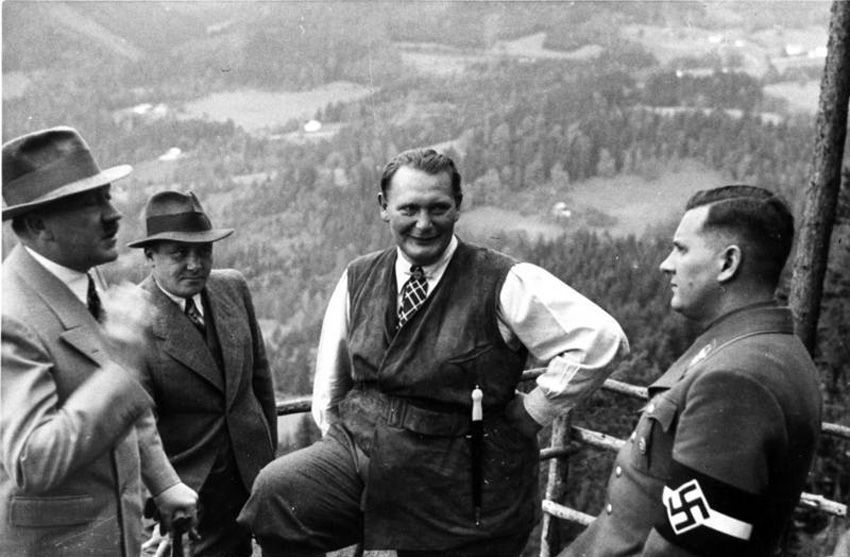 Schwarz-Weiß-Fotografie von vier Männern auf einer Aussichtsplattform. Einer in Uniform und Hakenkreuzbinde.