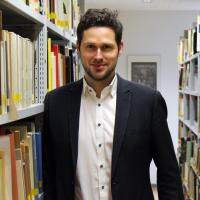 Mann steht zwischen zwei Bücherregalen