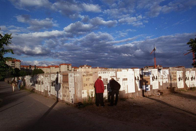 Baustelle des Holocaust-Mahnmals in Berlin, 1999, Fotograf: [http://www.gustfoto.de Dietmar Gust] ©, mit freundlicher Genehmigung. <br/>
1999 beschloss der Deutsche Bundestag, ein „Denkmal für die ermordeten Juden Europas“ in Berlin zu errichten. Über ein Jahrzehnt war öffentlich darüber gestritten worden, in den folgenden Jahren bis zur Eröffnung 2005 verlagerte sich die Diskussion aus dem Parlament an den Bauzaun. Argumente für und wider wurden jetzt direkt an den Zaun geklebt und geschrieben, und einige Beobachter schlugen vor, die Debatte selbst zum Mahnmal zu erklären. (Vgl. Jan-Holger Kirsch, Nationaler Mythos oder historische Trauer? Der Streit um ein zentrales „Holocaust-Mahnmal“ für die Berliner Republik, Köln 2003).