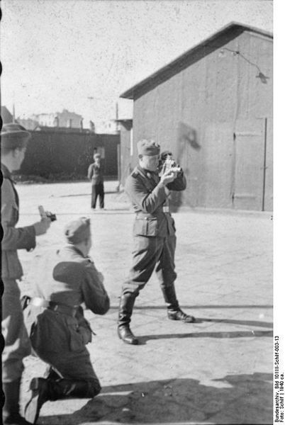 Ghetto Litzmannstadt, Polen, 1940: SS-Soldat einer Propaganda-Kompanie (PK-Filmberichter) bei der Aufnahme mit einer Filmkamera. Fotograf: Schilf, Quelle: [http://commons.wikimedia.org/wiki/File:Bundesarchiv_Bild_101III-Schilf-003-13,_Polen,_Ghetto_Litzmannstadt,_PK-Filmberichter.jpg?uselang=de. Wikimedia Commons/Bundesarchiv, Bild 101III-Schilf-003-13] ([https://creativecommons.org/licenses/by-sa/3.0/de/deed.en CC BY-SA 3.0 DE]).