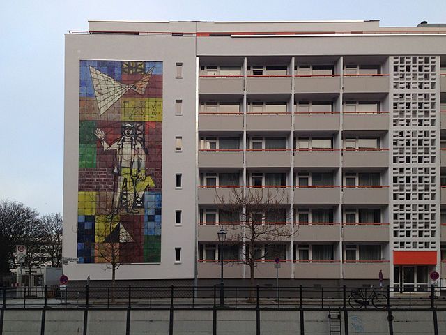 Das Wandmosaik von Walter Womacka „Der Mensch, das Maß aller Dinge“ nach seiner Umsetzung Berlin, Friedrichsgracht; ursprünglich am Ministerium für Bauwesen, Breite Straße. Fotograf: Achim Bodewig, Berlin 13. Dezember 2013. Quelle: [https://commons.wikimedia.org/wiki/File:Wandmosaik_womacka_der_mensch_das_mass_aller-dinge.jpg?uselang=de Wikimedia Commons], Lizenz: [https://creativecommons.org/licenses/by-sa/3.0/deed.de CC BY-SA 3.0]