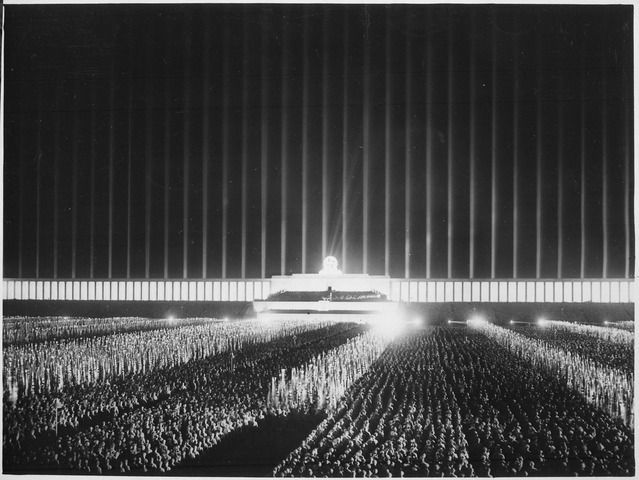 Reichsparteitag der NSDAP in Nürnberg 1937 auf der von Scheinwerfern bestrahlten Zeppelinwiese in Nürnberg: „Großer Appell der Politischen Leiter“. Fotograf: unbekannt, Quelle: National Archives and Records Administration / [https://commons.wikimedia.org/wiki/File:Reichsparteitag._Der_grosse_Appell_der_Politischen_Leiter_auf_der_von_Scheinwerfern_berstrahlten_Zeppelinwiese_in..._-_NARA_-_532605.tif  Wikimedia Commons], Lizenz: public domain