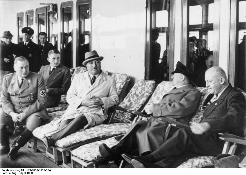 Der „Führer“ und sein Adlatus Robert Ley im April 1939 an Bord des KdF-Schiffes „Robert Ley“. Links außerdem Wilhelm Brückner (Chefadjutant Hitlers), rechts Adolf Wagner (NSDAP-Gauleiter für München-Oberbayern). Fotograf: unbekannt, Quelle: [https://commons.wikimedia.org/wiki/File:Bundesarchiv_Bild_183-2006-1128-504,_KdF-Schiff_%22Robert_Ley%22,_Adolf_Hitler_an_Bord.jpg Wikimedia Commons / Bundesarchiv, Bild 183-2006-1128-504], Lizenz: [https://creativecommons.org/licenses/by-sa/3.0/de/deed.en CC-BY-SA 3.0]