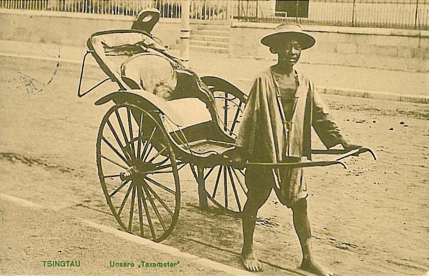 Postkarte aus der deutschen Kolonie Tsingtau (heute Qingdao) in China, ca. 1914. Die Rikscha kann in Anschluss an David Edgerton als eine „creole technology“ gedeutet werden, die lokale Technikanpassung und Techniknutzung erschließen lassen. Hier macht die Bildunterschrift „Unsere ‚Taxameter‘“ deutlich, wie koloniale Machtverhältnisse in technische Alltagsnutzungen eingeschrieben waren. Quelle: [https://de.wikipedia.org/wiki/Datei:Tsingtau_Taxameter_1914.jpg Wikimedia Commons], Lizenz: public domain