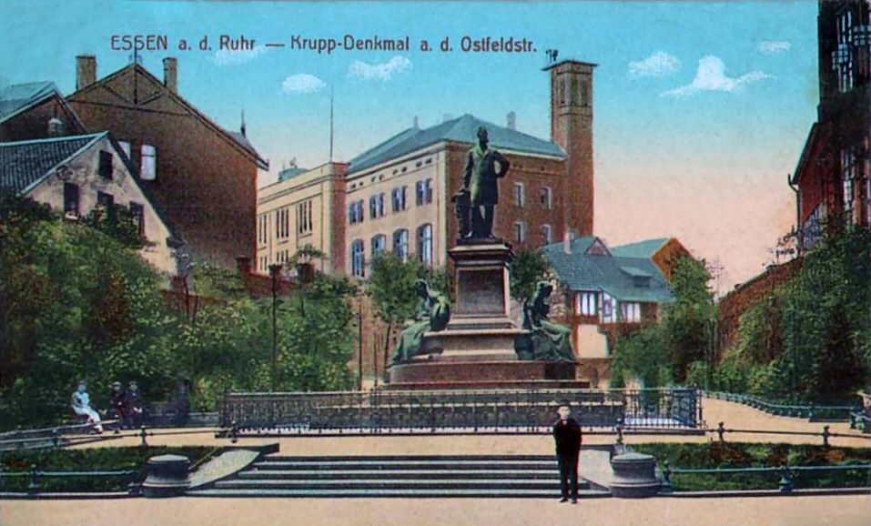 Patriarch im Kontext: Alfred-Krupp-Denkmal in Essen mit der Krupp'schen Konsumanstalt im Hintergrund, Ansichtskarte vor 1888. Quelle: [https://commons.wikimedia.org/wiki/File:Alfred-Krupp-Denkmal,_Konsumanstalt_Krupp1.JPG Wikimedia Commons], gemeinfrei