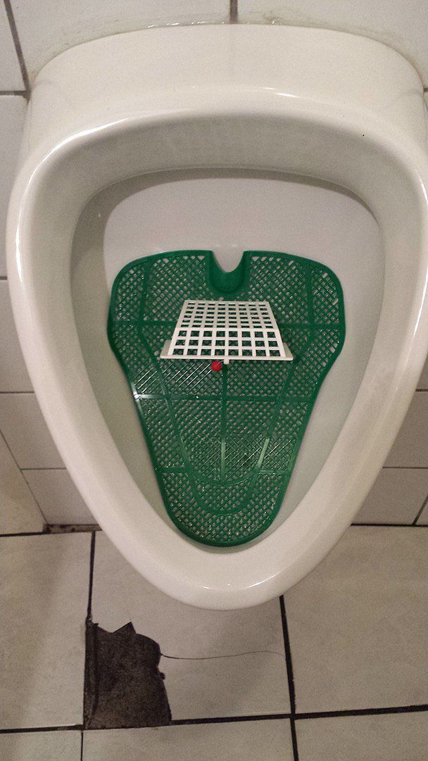 Mit der verhaltensökonomischen Technik des Nudging wird das Verhalten von Menschen in eine gewünschte Richtung gelenkt. Der Nudge (engl. Schubs, Stups) wird hier am Beispiel eines Urinals dargestellt, das mit einem Fußballfeld ausgestattet ist. Auf diese Weise wird der Nutzer zum Urinieren in das Fußballtor animiert und weniger Urin landet auf dem Boden. Grafik: WissensDürster, Quelle: [https://commons.wikimedia.org/wiki/File:Nudge_Urinal.jpg#/media/File:Nudge_Urinal.jpg Wikimedia Commons], Lizenz: [https://creativecommons.org/licenses/by-sa/4.0/deed.en CC BY-SA 4.0]