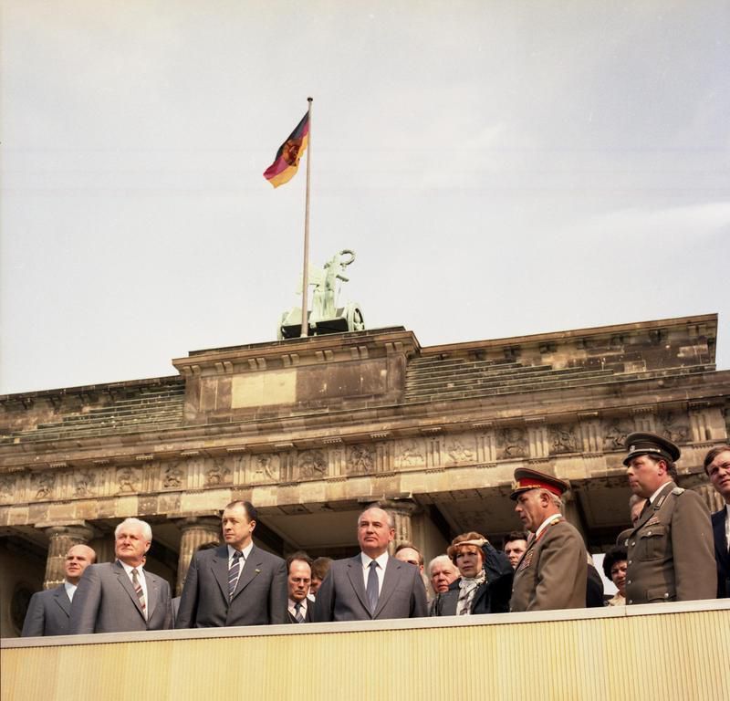 Zum XI. Parteitag der SED kam der Generalsekretär des ZK der KPdSU Michail Gorbatschow im April 1986 nach Ost-Berlin. Er sprach über Glasnost und Perestroika; die SED-Führung in der DDR gab sich unbeeindruckt. Das Bild zeigt Gorbatschow an der Mauer am Brandenburger Tor; links: Günter Mittag, Mitglied des Politbüros und Sekretär des ZK der SED; 2.v.r.: Stadtkommandant Generalleutnant Karl-Heinz Drews. Ost-Berlin, 16. April 1986. Foto: Hartmut Reiche (ADN-ZB). Quelle: [https://www.bild.bundesarchiv.de/dba/de/search/?query=Bild+183-1986-0416-418 Bundesarchiv Bild 183-1986-0416-418] / [https://commons.wikimedia.org/wiki/File:Bundesarchiv_Bild_183-1986-0416-418,_Berlin,_Michail_Gorbatschow_an_der_Mauer.jpg Wikimedia Commons], Lizenz: [https://creativecommons.org/licenses/by-sa/3.0/de/deed.en CC-BY-SA 3.0]