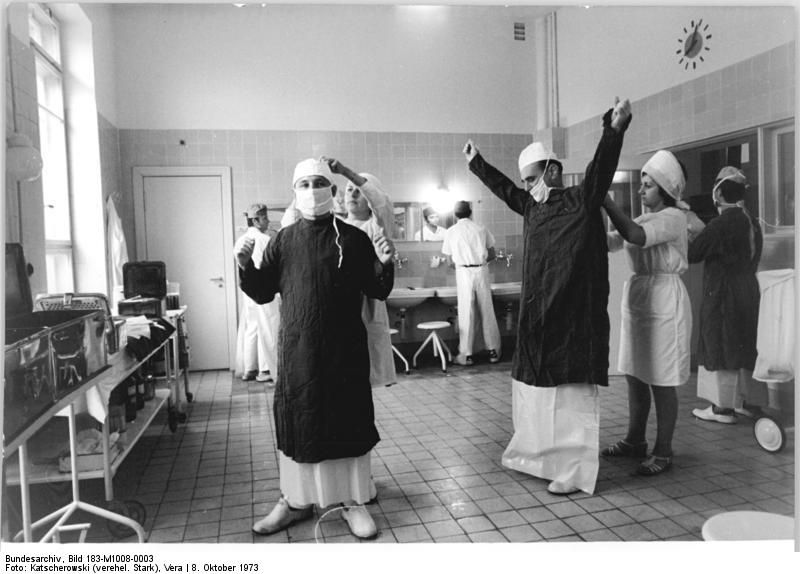 Operationsvorbereitung (in klassischer männlich-weiblicher Aufgabenverteilung) in der neu eingeweihten Frauenklinik der Charité, Berlin (Ost), 8. Oktober 1973.<br />Fotografin: Vera Katschorowski-Stark (ADN). Quelle: [https://www.bild.bundesarchiv.de/dba/de/search/?query=Bild+183-M1008-0003 Bundesarchiv Bild 183-M1008-003] / [https://commons.wikimedia.org/wiki/File:Bundesarchiv_Bild_183-M1008-0003,_Berlin,_Charit%C3%A9,_Frauenklinik,_Operation.jpg Wikimedia Commons], Lizenz: [https://creativecommons.org/licenses/by-sa/3.0/de/deed.en CC-BY-SA 3.0]